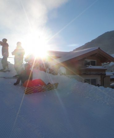 Skifahrer und Snowboarder starten in den Tag direkt vor dem Appartementhaus Casamarai in Saalbach. Perfekt präparierte Pisten, Ski in & Ski out und die aufgehende Sonne schaffen die ideale Atmosphäre für einen unvergesslichen Winterurlaub in den Alpen.